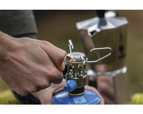 Eine Person zündet einen Campingkocher an, auf dem eine Espressokanne steht.