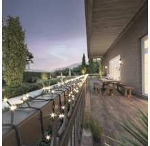Terrasse mit Lichterkette am Geländer, Tisch und Bänken im Hintergrund.