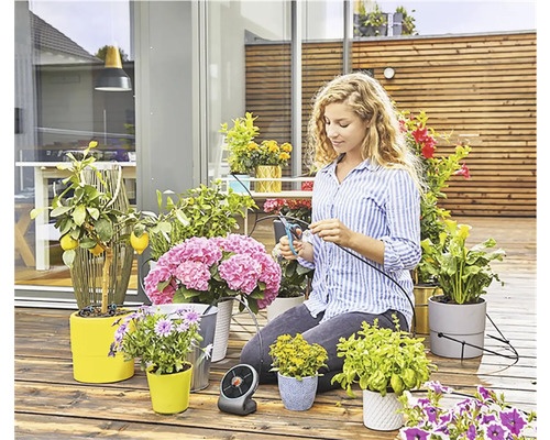 Frau schneidet Bewässerungsschlauch für Pflanzen auf einer Terrasse