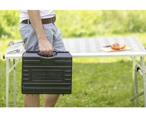 Person trägt Campingaz Grill im Transportkoffer im Garten