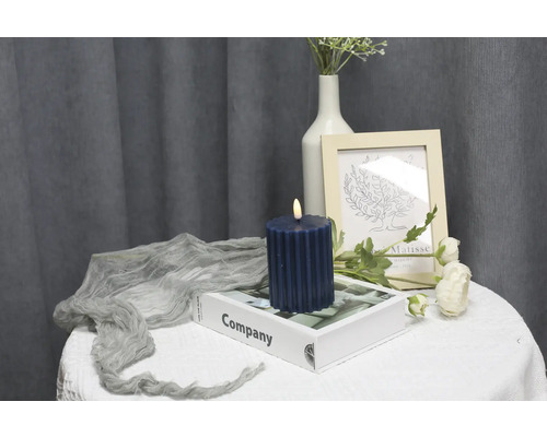 Scène décorative avec bougie pilier cannelée, livre, cadre photo et fleurs sur une table