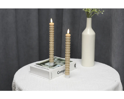 Zwei dekorative LED-Kerzen mit Batteriebetrieb, auf einem Tisch mit Buch und Vase