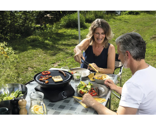 Szene im Freien mit einem Paar beim Grillen mit einem Tischgrill, Grillgut, Salaten und Getränken