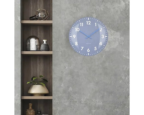 Eine blaue Wanduhr mit einem Zifferblatt hängt an einer grauen Wand neben einem Holzregal.