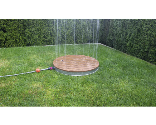 Runder Rasensprenger aus Holz und Metall auf einer Rasenfläche im Garten.