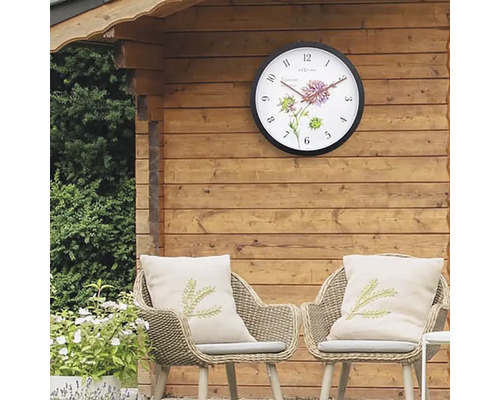 Gartenszene mit Wanduhr an Holzwand und zwei Rattansesseln mit Kissen