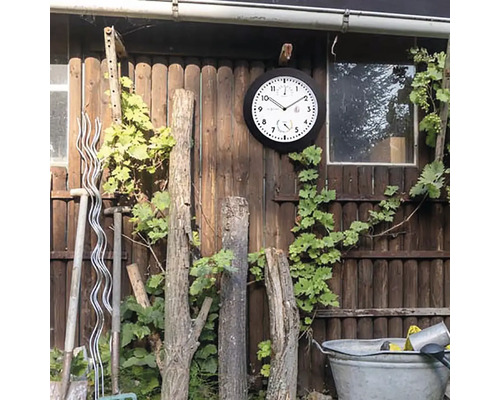 Außenszene mit Wanduhr, Weinpflanze, Gartengeräten und Holzzaun