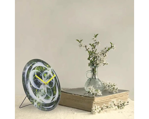 Horloge de table décorative avec un design abstrait et des aiguilles jaunes à côté d''un livre et d''un vase avec des fleurs blanches.