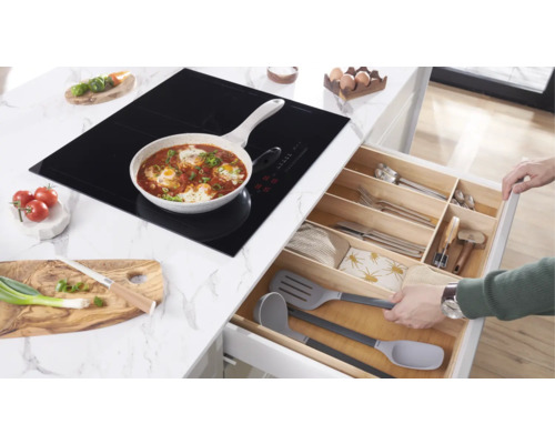 Kochszene mit Induktionskochfeld, Pfanne mit Essen und geöffneter Küchenschublade mit Besteck