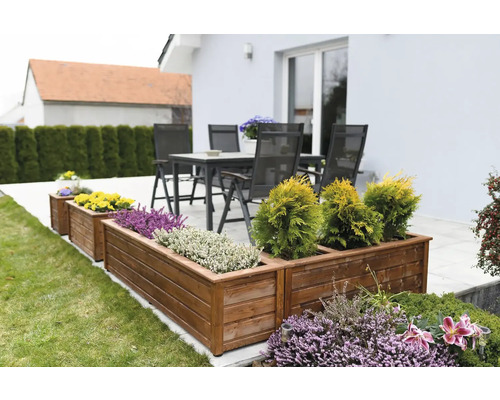 Holzpflanzkästen mit verschiedenen Pflanzen im Garten und Terrassenmöbel im Hintergrund.