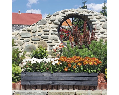Dekorativer Garten mit Blumenkasten aus Holz, Mauer aus Steinen und Wagenrad