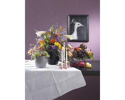 Nature morte décorative avec arrangements floraux, bougies et fruits sur une table avec une nappe blanche devant un mur avec une image encadrée