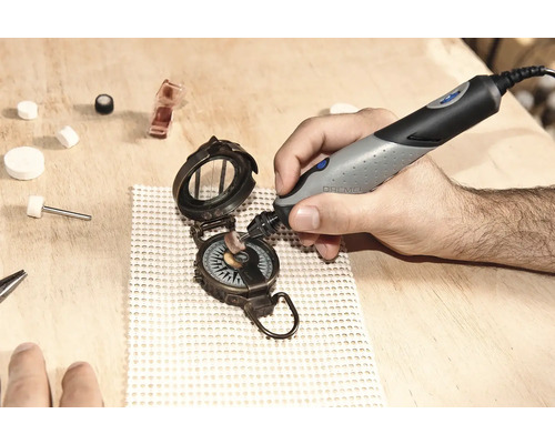 Main polissant un compas avec un outil Dremel sur une surface en bois