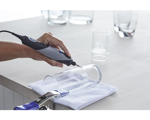 Logo Dremel. Main meulant un verre avec un outil multifonction Dremel. Le verre est fixé avec une pince.