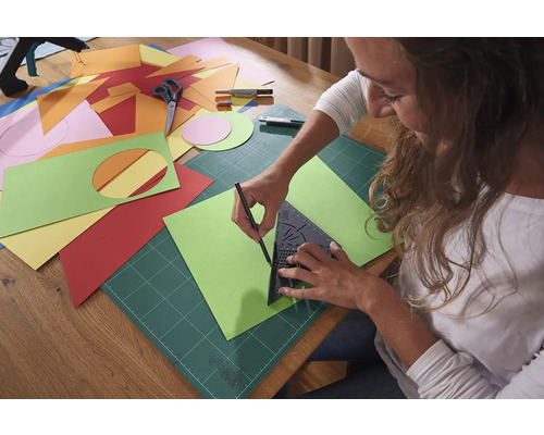 Frau zeichnet eine grüne Papiervorlage mit einem Dreieck, einer Schneidematte und einem Bleistift.