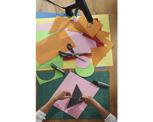 Bastelszene mit Papier, Schere, Klebepistole und Schneidematte