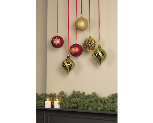 Boules de Noël décoratives suspendues à des rubans rouges au-dessus d''un manteau de cheminée avec une guirlande de sapin et des bougies