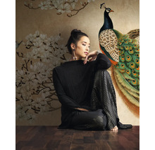 Femme assise devant un papier peint photo avec motif paon et fleurs.