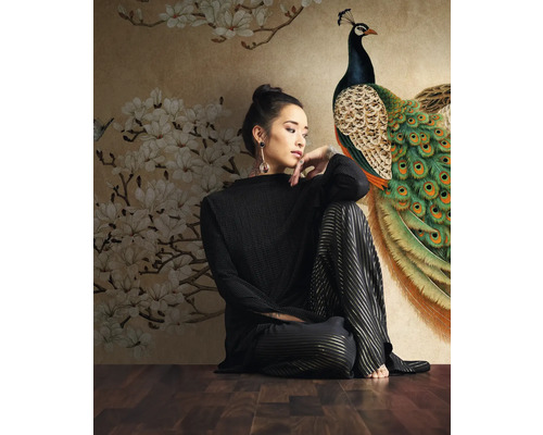 Femme assise devant un papier peint photo avec motif paon et fleurs.