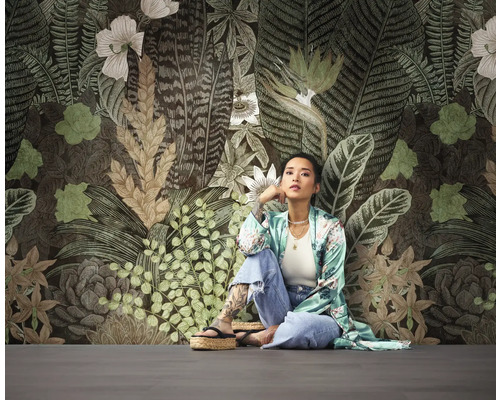 Frau sitzt vor einer Wand mit floralem Tapetenmuster