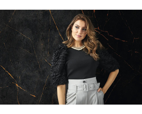 Frau mit schwarzem Oberteil und grauer Hose vor Marmorwand