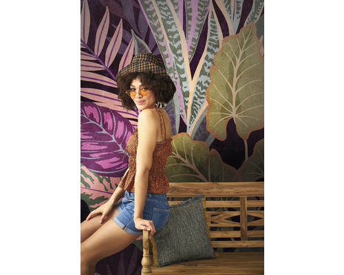 Une femme est assise sur un banc en bois devant un papier peint à motifs de jungle.