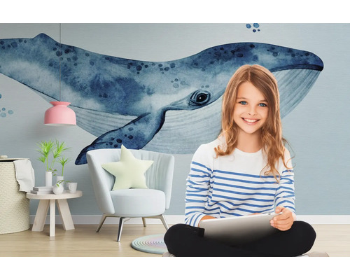 Fille avec tablette devant un papier peint photo avec motif de baleine, un fauteuil, une table d''appoint et une lampe.