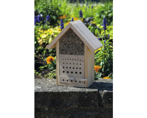 Insektenhotel aus Holz mit verschiedenen Nistmöglichkeiten vor Blumenbeet