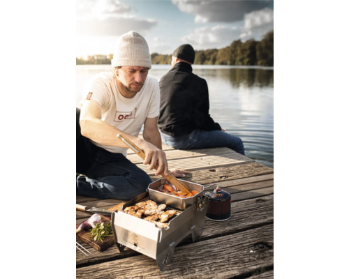 Szene mit einem Mann, der auf einem tragbaren Grill am See grillt