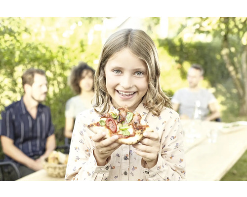 Fille tenant une pizza dans le jardin, famille en arrière-plan
