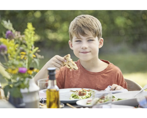Un garçon mange à une table dressée à l''extérieur.