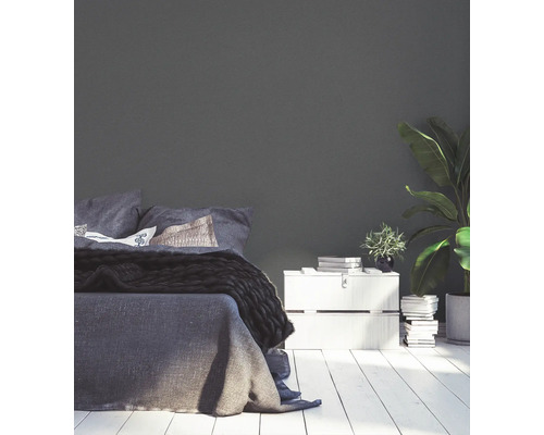 Schlafzimmer mit Bett, Nachttisch und Zimmerpflanze vor einer einfarbigen Wand