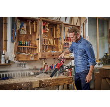 Un homme utilise un aspirateur de feuilles sans fil pour souffler les copeaux d''un établi. Outils en arrière-plan dans une armoire.