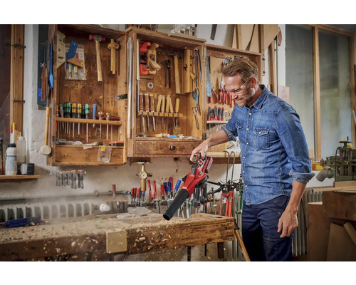 Un homme utilise un aspirateur de feuilles sans fil pour souffler les copeaux d''un établi. Outils en arrière-plan dans une armoire.
