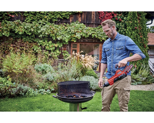 Un homme utilise un allume-barbecue dans un jardin.
