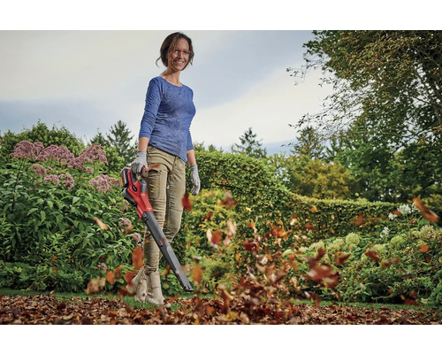 Une femme utilise un souffleur de feuilles sans fil dans le jardin pour enlever les feuilles.