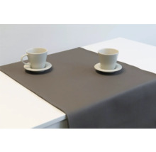 Grauer Tischläufer aus Lederimitat mit zwei Kaffeetassen auf einem weißen Tisch.