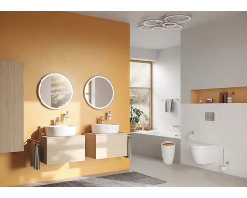 Badezimmer mit Doppelwaschtisch, runden Spiegeln mit Beleuchtung, Badewanne und Toilette.