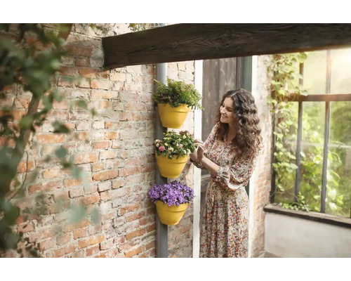 Frau betrachtet Pflanzgefäße mit Blumen an einer Hauswand.