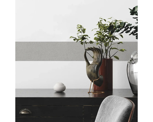 Accessoires décoratifs sur une commode noire devant un mur à rayures grises et blanches