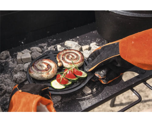 Zwei Spiralwürste und Gemüse auf einem Grillrost mit Grillhandschuh