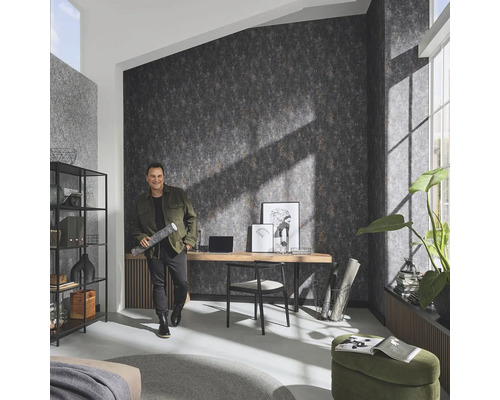 Wohnraum mit Mustertapete, Schreibtisch und Mann mit Tapetenrolle