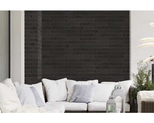 Wohnbereich mit Wandverkleidung aus schwarzen Ziegelsteinen und weißem Sofa mit Kissen