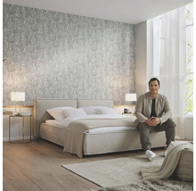 Helles Schlafzimmer mit gemusterter Tapete, Doppelbett, Teppich und sitzendem Mann