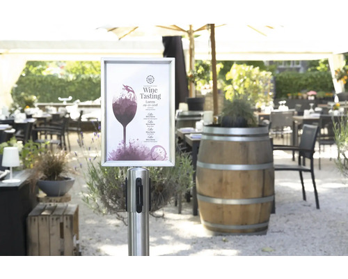 Außenbereich eines Restaurants mit Weinprobe Ankündigungsplakat, Holztischen und Stühlen.