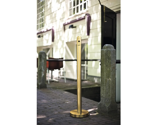 Goldfarbener Poller mit Zigarettenstummel-Symbol auf einem Ziegelweg