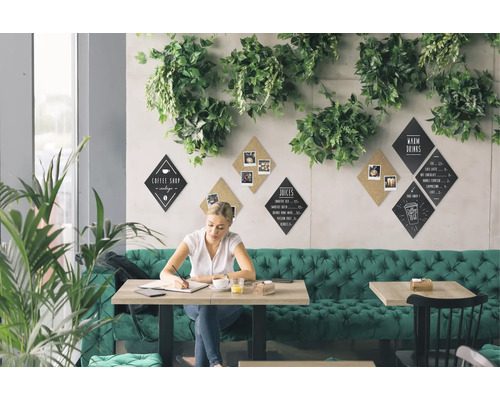 Szene eines hellen Cafés mit grüner Dekoration, in dem eine Frau an einem Tisch sitzt und schreibt