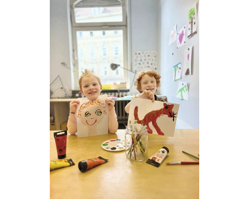 Zwei Kinder präsentieren stolz ihre mit Farbe gemalten Bilder.