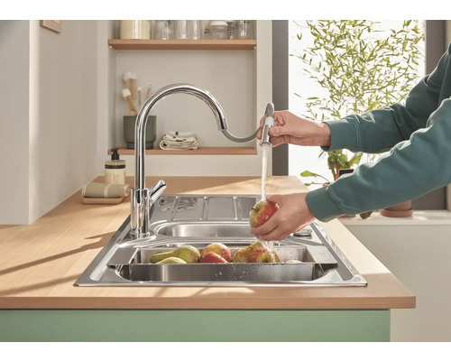 Spültisch mit Wasserhahn und Person beim Abwaschen von Obst in der Küche