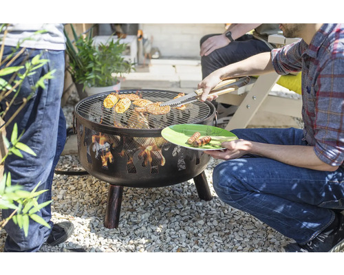 Brasero avec grille de barbecue dans le jardin, avec des aliments grillés et une personne tenant une pince à barbecue